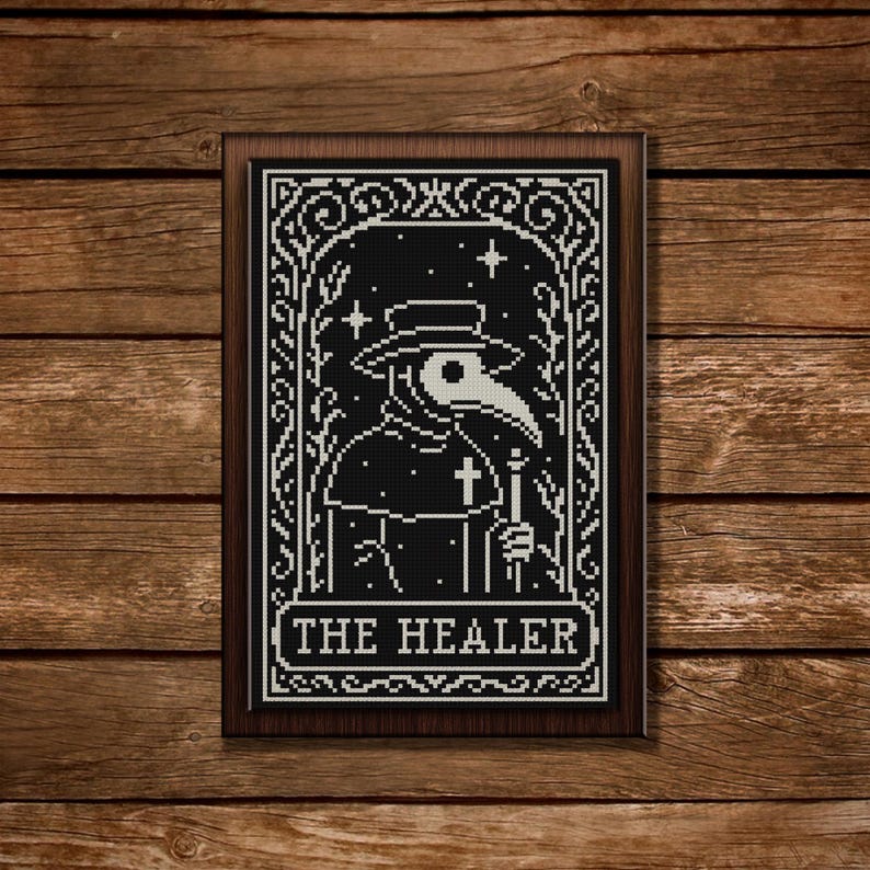 May include: A framed black and white cross-stitch depicting a plague doctor with a long beak, holding a staff and cross. The text "THE HEALER" is at the bottom. The artwork is set against a wooden background.