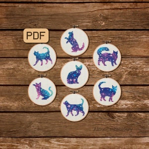 Puede incluir: Seis patrones de bordado en forma de aro que representan gatos con temática de galaxia en varias poses. Los aros son blancos con un marco de madera. El texto PDF es visible en la esquina superior izquierda.