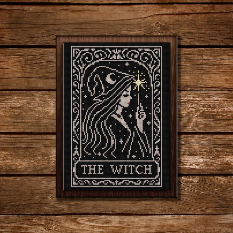 May include: Cross-stitch artwork of a witch with long hair, a crescent moon, and a star. The black and white design is framed in a dark wood frame. The text "THE WITCH" is at the bottom of the image.