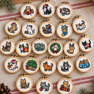 Op de afbeelding: Een verzameling van eenentwintig kleine, ronde houten borduurringen, elk met een uniek kruissteekontwerp van een kat in verschillende kerstthema's, waaronder katten met kerstbomen, cadeautjes, kerstsokken en truien.