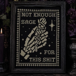 May include: A framed cross-stitch embroidery on black fabric featuring a pale yellow design of two hands pressed together in prayer. The text reads NOT ENOUGH SAGE FOR THIS SHIT, surrounded by a decorative border and small star-like accents.