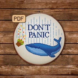 Könnte beinhalten: Ein Kreuzstichmuster mit einem blauen Wal mit dem Text "DON'T PANIC" und einem Blumentopf. Das Muster ist in einem Holzreifen gerahmt.