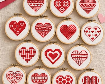 May include: A collection of fourteen circular wooden embroidery hoops, each containing white fabric with a unique red cross-stitch heart pattern. The hearts feature various geometric, floral, and grid-like designs in red thread.