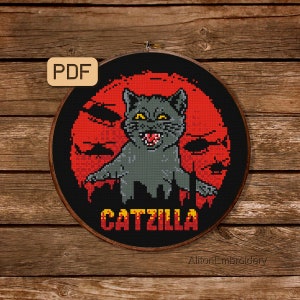 May include: Cross stitch pattern featuring a black cat with yellow eyes and a red background. The cat is depicted as a monster with the text "CATZILLA" below it. The pattern is for a round embroidery hoop.