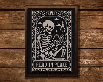 May include: Black and white cross-stitch framed art featuring a skeleton reading a book. The skeleton is seated, with a church in the background. The text "READ IN PEACE" is at the bottom.
