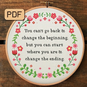 以下が含まれることがあります： 花柄の縁取りが施された白い刺繍枠に、「You can't go back & change the beginning, but you can start where you are & change the ending.」という引用が書かれています。