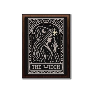 May include: Cross-stitch art of a witch with long hair, a hat, and a wand, set against a black background. The image is framed in a dark wood frame, with the words "THE WITCH" at the bottom.