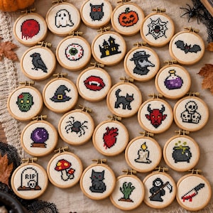 May include: A collection of small circular wooden embroidery hoops featuring various Halloween-themed cross-stitch designs, including a ghost, pumpkin, spider web, bat, skull, vampire lips, black cat, raven, heart, and other spooky icons on white fabric.