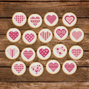 Könnte beinhalten: Eine Sammlung von 18 kleinen, runden Stickrahmen mit verschiedenen rosa Herzmustern. Die Herzen weisen unterschiedliche Muster auf, darunter Vichy, Streifen und geometrische Formen. Die Rahmen sind auf einer Holzoberfläche angeordnet.