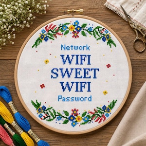 Może przedstawiać: Okrągła haftowana obręcz z krzyżykami z niebieskim napisem "Network WIFI SWEET WIFI Password". Wzór otoczony jest kwiatową obwódką z niebieskimi, żółtymi i czerwonymi kwiatami i zielonymi liśćmi. Widoczne są również nici do haftu w różnych kolorach.