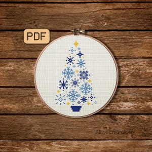 May include: A cross-stitch design of a Christmas tree in a round embroidery hoop. The tree is composed of blue and yellow snowflakes on a white background. The hoop is set against a wooden background. The PDF text is in the upper left corner.