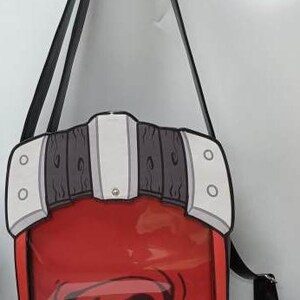 Puede incluir: Bolso bandolera rojo y transparente con correa negra. El bolso tiene un dise&ntilde;o &uacute;nico con detalles en blanco, gris y negro, y un gr&aacute;fico en el centro. El bolso est&aacute; dise&ntilde;ado para llevarse al hombro.