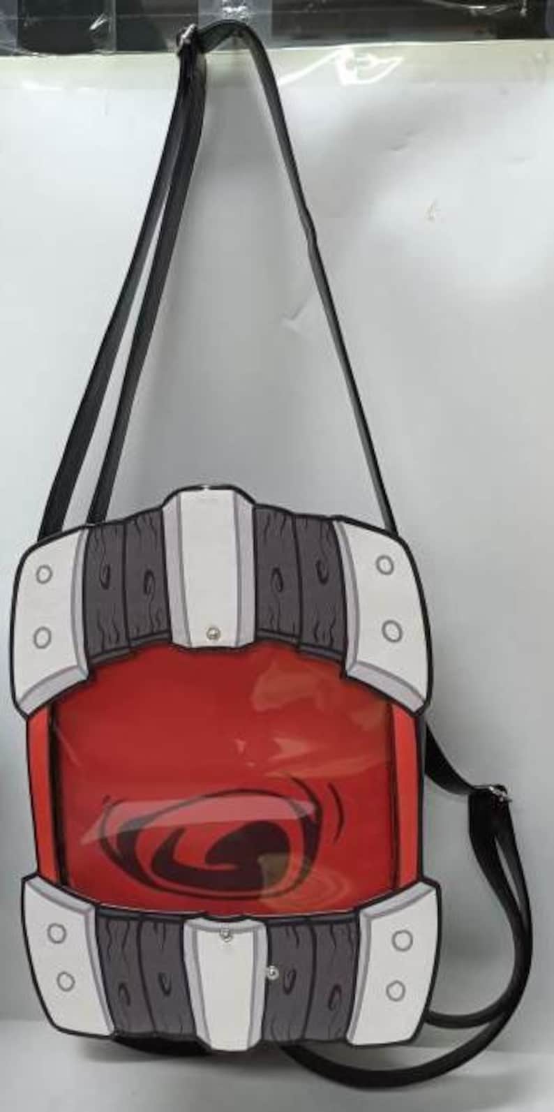 Puede incluir: Bolso bandolera rojo y transparente con correa negra. El bolso tiene un dise&ntilde;o &uacute;nico con detalles en blanco, gris y negro, y un gr&aacute;fico en el centro. El bolso est&aacute; dise&ntilde;ado para llevarse al hombro.