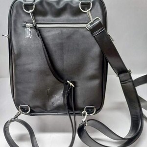 Puede incluir: Mochila negra con herrajes plateados. La mochila tiene forma rectangular, correas ajustables y un asa superior. Un bolsillo con cremallera es visible en la parte delantera. La palabra "Hunnys" est&aacute; grabada en la parte posterior.