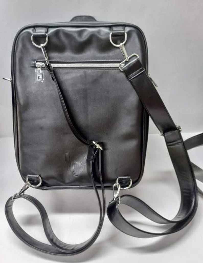 Puede incluir: Mochila negra con herrajes plateados. La mochila tiene forma rectangular, correas ajustables y un asa superior. Un bolsillo con cremallera es visible en la parte delantera. La palabra "Hunnys" est&aacute; grabada en la parte posterior.