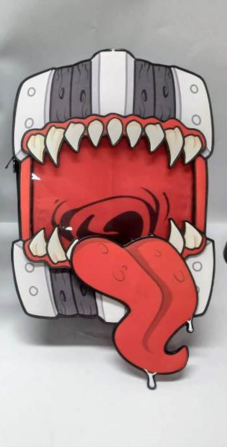 Puede incluir: Una mochila novedosa con forma de boca abierta de un monstruo de dibujos animados. El dise&ntilde;o presenta un interior rojo, dientes blancos y una larga lengua roja. El exterior tiene una combinaci&oacute;n de colores gris y blanco.