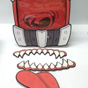 Puede incluir: Un accesorio de boca rojo y caricaturesco con una ventana de pl&aacute;stico transparente, detalles grises y blancos y paneles con aspecto de madera. Incluye dientes de cart&oacute;n separados y una lengua roja con detalles goteantes. Ideal para Halloween o uso teatral.