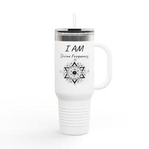 May include: White travel mug with a handle and a straw. The mug features the text "I AM Divine Frequency" above a black and white geometric design. The mug is designed to keep beverages hot or cold.
