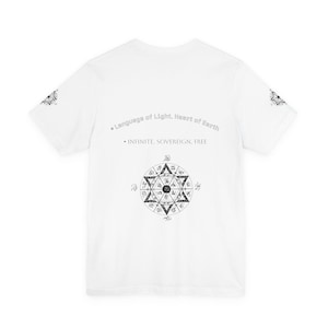 May include: White t-shirt with a circular geometric design and text that reads "Language of Light, Heart of Earth" and "INFINITE, SOVEREIGN, FREE". The design is in shades of gray and black.