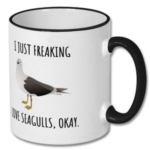 May include: White ceramic coffee mug with a black rim and handle. The mug has a black and white illustration of a seagull and the text "I just freaking love seagulls, okay."