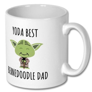May include: White ceramic coffee mug with a green cartoon Yoda character holding a walking stick. The text "Yoda Best Bernedoodle Dad" is printed on the mug.