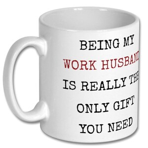May include: White ceramic mug with a curved handle. The mug features the text "BEING MY WORK HUSBAND IS REALLY THE ONLY GIFT YOU NEED" in black and red lettering.