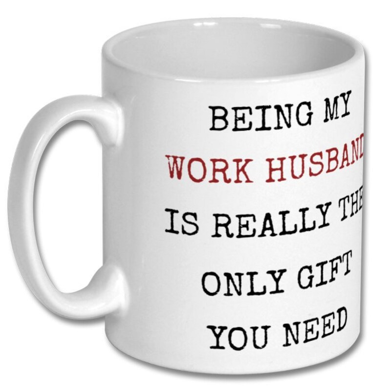 May include: White ceramic mug with a curved handle. The mug features the text "BEING MY WORK HUSBAND IS REALLY THE ONLY GIFT YOU NEED" in black and red lettering.