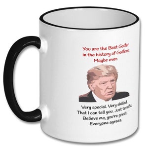 May include: White ceramic coffee mug with a black rim and handle. The mug features a cartoon image of a man with the text "You are the Best Golfer in the history of Golfers. Maybe ever. Very special. Very skilled. That I can tell you. Just terrific. Believe me, you're great. Everyone agrees."