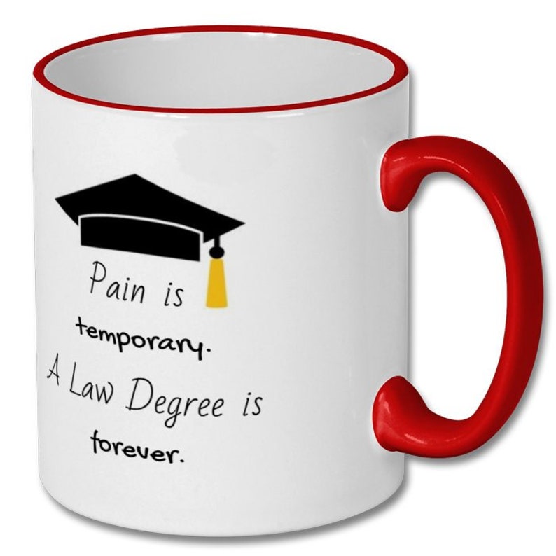 May include: White ceramic mug with a red interior and handle. The mug features a black graduation cap graphic with a yellow tassel and the text "Pain is temporary. A Law Degree is forever."