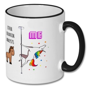 May include: White coffee mug with a black rim and handle. The mug features a cartoon unicorn on a pole dancing, with the text "OTHER BEHAVIOR ANALYSTS" on the left and "ME" in pink letters on the right.