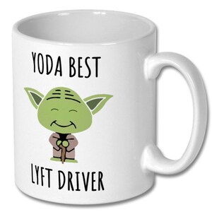 May include: White ceramic mug with a green cartoon character of Yoda from Star Wars. The mug has the text "Yoda Best Lyft Driver" printed on it.