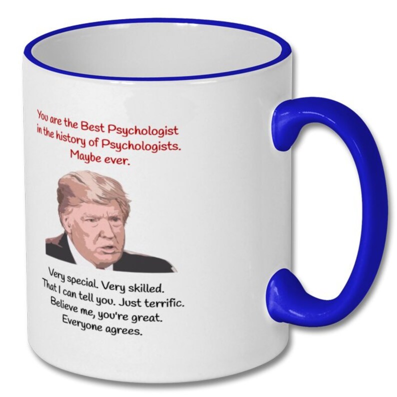 May include: White ceramic coffee mug with a blue rim and handle. The mug features a cartoon image of Donald Trump and text that reads "You are the Best Psychologist in the history of Psychologists. Maybe ever. Very special. Very skilled. That I can tell you. Just terrific. Believe me, you're great. Everyone agrees."