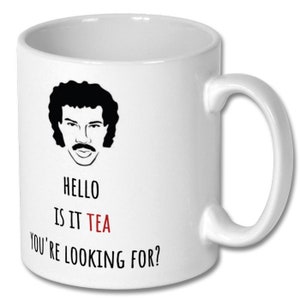 May include: White ceramic mug featuring a black and white illustration of a man with a moustache and afro. The text "HELLO IS IT TEA YOU'RE LOOKING FOR?" is printed on the mug, with the word "TEA" in red.