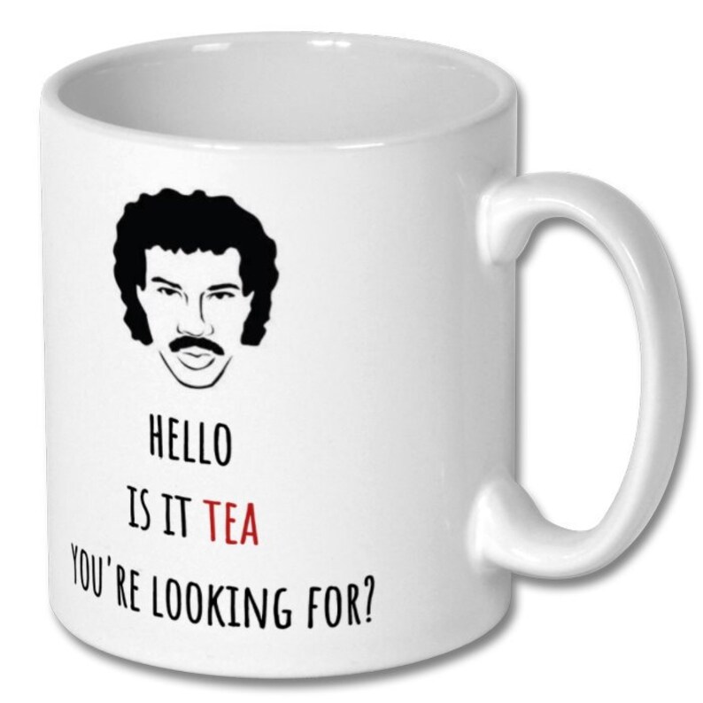 May include: White ceramic mug featuring a black and white illustration of a man with a moustache and afro. The text "HELLO IS IT TEA YOU'RE LOOKING FOR?" is printed on the mug, with the word "TEA" in red.