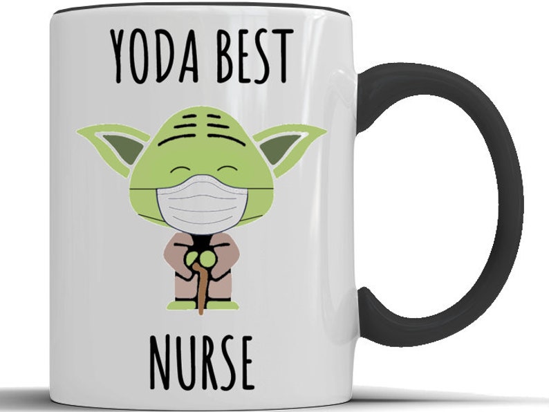 K&ouml;nnte beinhalten: Eine wei&szlig;e Keramiktasse mit schwarzem Henkel. Die Tasse zeigt ein Cartoon-Bild von Yoda, der eine Gesichtsmaske tr&auml;gt und einen Gehstock h&auml;lt. Der Text "YODA BEST NURSE" ist auf die Tasse gedruckt.