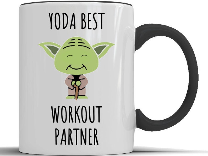 May include: White ceramic mug with a black handle. The mug features a cartoon image of Yoda from Star Wars with the text "YODA BEST WORKOUT PARTNER".