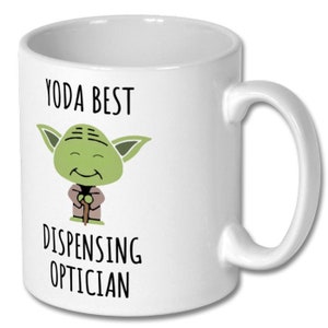 May include: White ceramic coffee mug with a green cartoon character holding a stick. The text on the mug reads "Yoda Best Dispensing Optician".