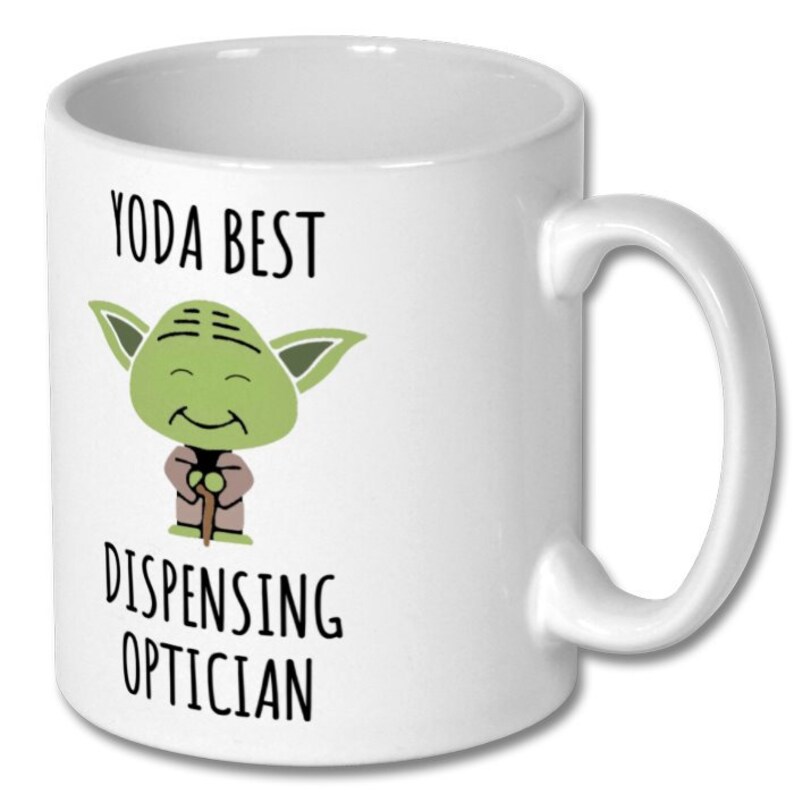 May include: White ceramic coffee mug with a green cartoon character holding a stick. The text on the mug reads "Yoda Best Dispensing Optician".