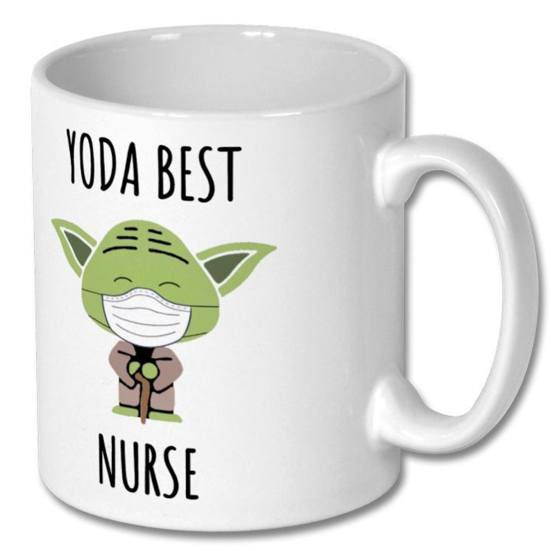 K&ouml;nnte beinhalten: Wei&szlig;e Keramiktasse mit einer gr&uuml;nen Comicfigur, die eine Gesichtsmaske tr&auml;gt und einen Stock h&auml;lt. Der Text "YODA BEST NURSE" ist auf die Tasse gedruckt.