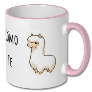May include: White ceramic coffee mug with a pink rim and handle. The mug features a cartoon illustration of a white llama with the text "C&oacute;mo te" printed on the front.