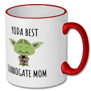 May include: White ceramic mug with a red rim and handle. The mug features a cartoon image of Yoda from Star Wars with the text "Yoda Best Surrogate Mom".