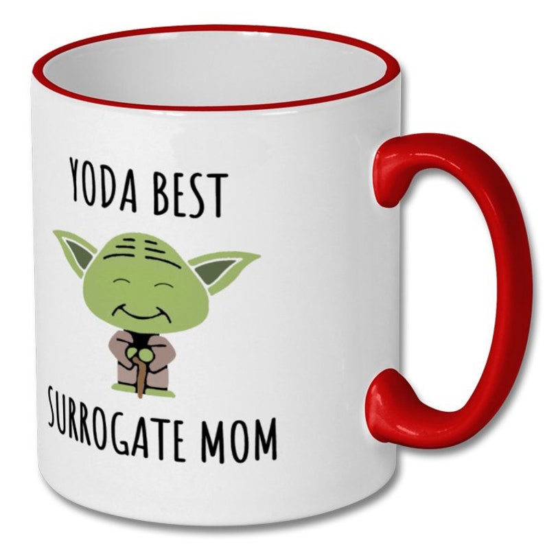 May include: White ceramic mug with a red rim and handle. The mug features a cartoon image of Yoda from Star Wars with the text "Yoda Best Surrogate Mom".