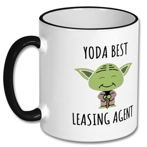 May include: White ceramic coffee mug with a black rim and handle. The mug features a cartoon image of Yoda from Star Wars with the text "Yoda Best Leasing Agent".