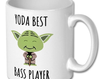 May include: White ceramic mug featuring a cartoon image of Yoda with the text "YODA BEST BASS PLAYER" in black. The Yoda character is green with large ears and a brown robe.
