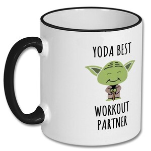 May include: White ceramic coffee mug with a black rim and handle. The mug features a cartoon image of Yoda from Star Wars with the text "Yoda Best Workout Partner".