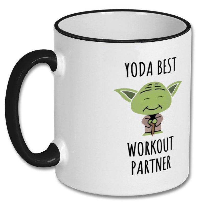 May include: White ceramic coffee mug with a black rim and handle. The mug features a cartoon image of Yoda from Star Wars with the text "Yoda Best Workout Partner".