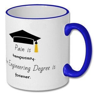Op de afbeelding: Witte keramische koffiemok met een blauwe rand en handvat. De mok heeft een zwarte graduatiecap met een gele kwast en de tekst "Pijn is tijdelijk. Een ingenieursdiploma is voor altijd."