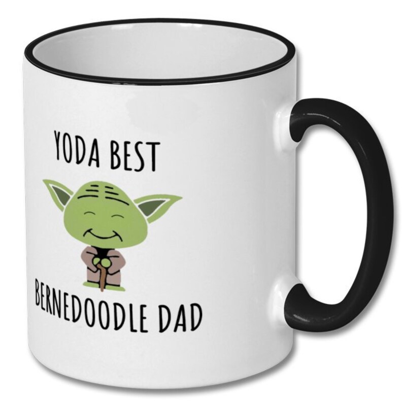 May include: White ceramic coffee mug with a black rim and handle. The mug features a cartoon image of Yoda from Star Wars, with the text "Yoda Best Bernedoodle Dad".