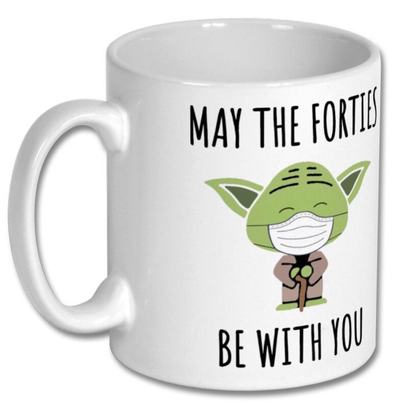 May include: White ceramic mug with a green Yoda character wearing a face mask. The text on the mug reads "May the Forties Be With You".