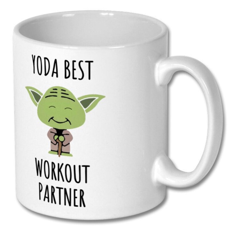 May include: White ceramic coffee mug with a green cartoon character of Yoda from Star Wars. The text on the mug reads "Yoda Best Workout Partner".